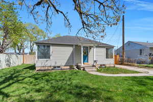 Bungalow-style home with a front yard, fence, and a shingled roof
