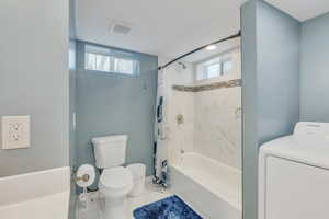 Bathroom featuring washer / clothes dryer, shower / tub combo, toilet, and a healthy amount of sunlight