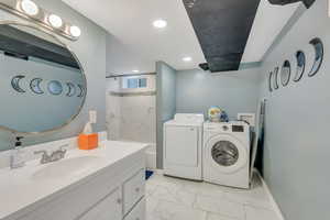 Washroom featuring laundry area, marble finish floor, a sink, baseboards, and washing machine and dryer