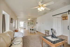 Carpeted living area featuring wooden walls, ceiling fan, arched walkways, and a barn door
