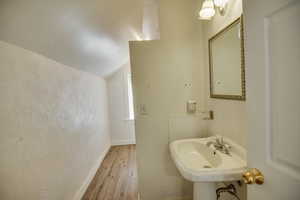 Bathroom with baseboards, vaulted ceiling, a textured wall, a sink, and wood finished floors