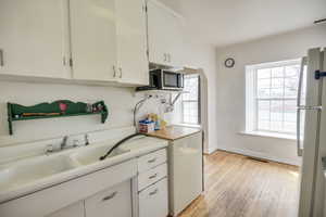 Kitchen with white cabinets, baseboards, light wood-type flooring, freestanding refrigerator, and stainless steel microwave