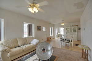 Living room with light wood finished floors, a ceiling fan, light carpet, and a healthy amount of sunlight