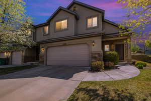 Traditional-style house with a garage, driveway, stucco siding, and stone siding
