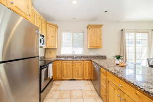Kitchen featuring a sink, light tile patterned floors, dark stone counters, and stainless steel appliances