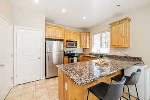 Kitchen featuring dark stone countertops, a sink, a kitchen bar, a peninsula, and stainless steel appliances