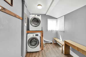 Washroom featuring stacked washing maching and dryer, wood finished floors, and laundry area