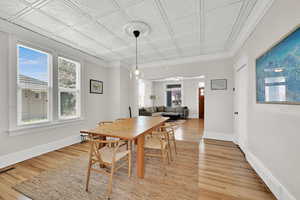 Dining space with crown molding, refinished hardwood floors, baseboards, and an ornate ceiling