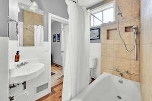 Bathroom featuring shower / bath combination with curtain, visible vents, wood finished floors, wainscoting, and tile walls