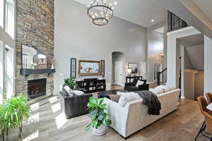 Living room with arched walkways, an inviting chandelier, a fireplace, a towering ceiling, and wood-type flooring