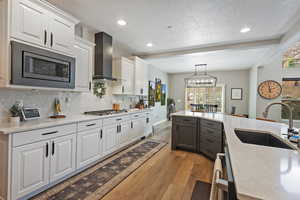 Kitchen with wall chimney exhaust hood, white cabinets, appliances with stainless steel finishes, light countertops, and a sink