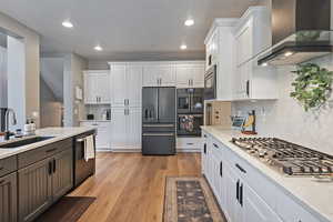 Kitchen with high end fridge, wall chimney range hood, stainless steel gas cooktop, dishwashing machine, and a sink