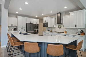 Kitchen with wall chimney exhaust hood, a sink, black appliances, recessed lighting, and white cabinetry