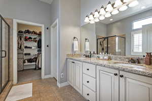 Bathroom featuring a sink, a walk in closet, a shower stall, and double vanity