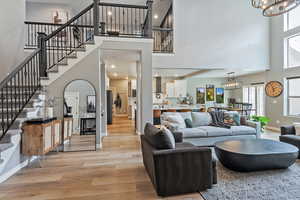 Living room featuring a notable chandelier, a towering ceiling, baseboards, light wood-style flooring, and stairs