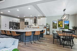Kitchen featuring a sink, wall chimney range hood, light wood-type flooring, black appliances, and white cabinetry