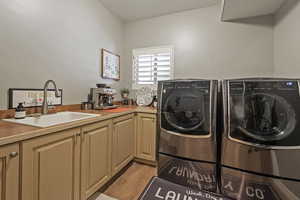 Laundry area with light wood-type flooring, a sink, cabinet space, and washing machine and dryer