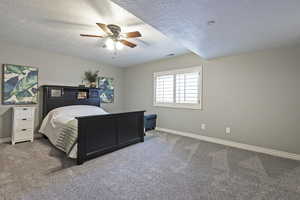 Carpeted bedroom with visible vents, baseboards, ceiling fan, and a textured ceiling