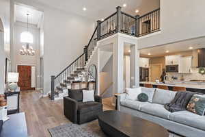 Living area featuring a towering ceiling, baseboards, light wood-type flooring, an inviting chandelier, and stairway