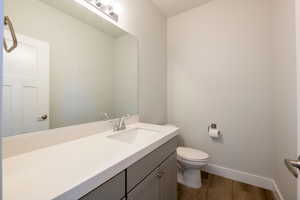 Half bathroom with toilet, wood finished floors, vanity, and baseboards