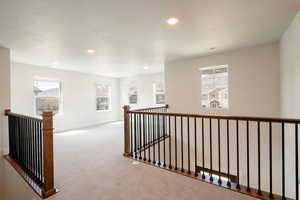 Hall featuring an upstairs landing, carpet flooring, and plenty of natural light