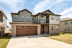 View of front of house featuring concrete driveway, a balcony, stone siding, a front lawn, and an attached garage