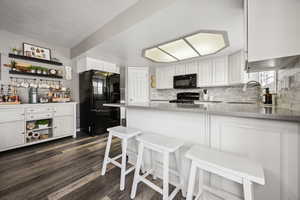 Kitchen with backsplash, a sink, open shelves, and black appliances