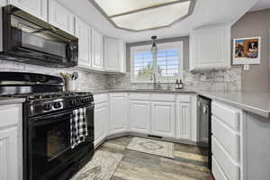 Kitchen with tasteful backsplash, a sink, white cabinetry, and black appliances