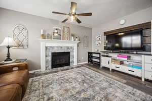 Living room with baseboards, a ceiling fan, a premium fireplace, and wood finished floors