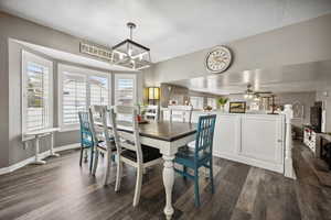 Dining area featuring dark wood-type flooring, a textured ceiling, ceiling fan with notable chandelier, and baseboards