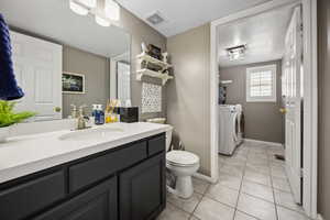 Bathroom featuring vanity, visible vents, toilet, washing machine and clothes dryer, and tile patterned floors