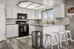 Kitchen featuring a sink, white cabinets, black appliances, and dark wood finished floors