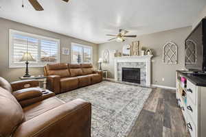 Living area with dark wood-type flooring, ceiling fan, a high end fireplace, and baseboards