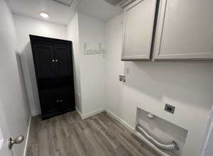Clothes washing area featuring light wood-style floors, electric dryer hookup, baseboards, and cabinet space