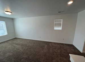 Spare room with dark carpet, visible vents, baseboards, and a textured ceiling