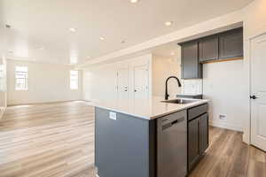 Kitchen featuring an island with sink, light wood-type flooring, dishwasher, light countertops, and a sink