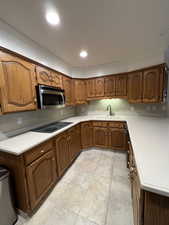 Kitchen featuring ornamental molding, stainless steel microwave, a sink, black electric stovetop, and brown cabinets