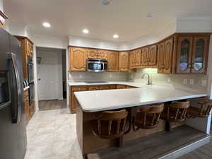 Kitchen featuring a peninsula, appliances with stainless steel finishes, light countertops, a sink, and brown cabinets