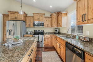 Kitchen featuring appliances with stainless steel finishes, dark stone countertops, dark wood-type flooring, lofted ceiling, and a sink