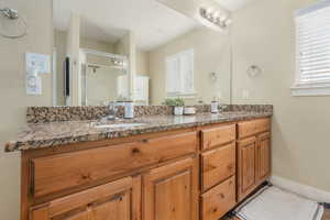 Full bathroom featuring a shower stall, double vanity, a sink, and baseboards