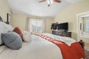 Bedroom with ceiling fan, connected bathroom, and lofted ceiling