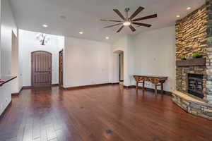 Unfurnished living room featuring ceiling fan with notable chandelier, arched walkways, a stone fireplace, recessed lighting, and dark wood-style flooring