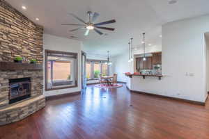 Living room featuring a fireplace, dark wood-style floors, ceiling fan with notable chandelier, and baseboards