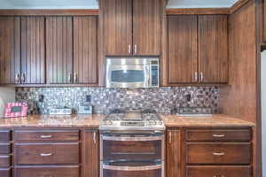 Kitchen featuring stainless steel appliances, light stone counters, and decorative backsplash