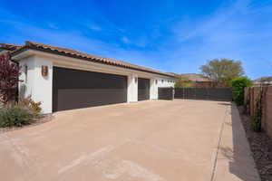 View of property exterior with a tiled roof, fence, concrete driveway, stucco siding, and a gate