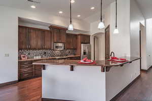 Kitchen with stainless steel appliances, dark brown cabinetry, a kitchen breakfast bar, and decorative backsplash