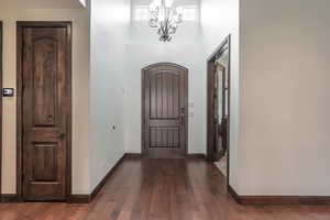 Foyer entrance featuring baseboards, an inviting chandelier, a towering ceiling, and dark wood-style floors