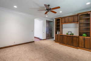 Unfurnished living room with crown molding, ceiling fan, carpet, arched walkways, and baseboards