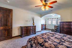 Bedroom with visible vents, baseboards, arched walkways, ornamental molding, and light carpet