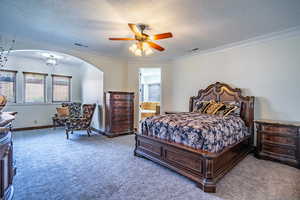Carpeted bedroom featuring arched walkways, crown molding, and visible vents
